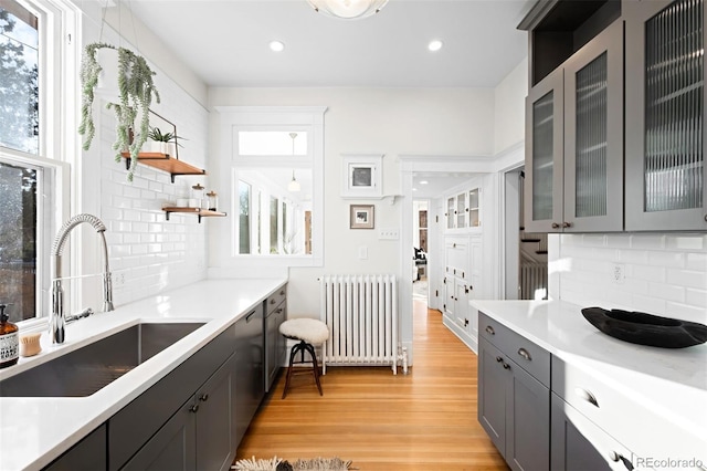 kitchen featuring radiator, decorative light fixtures, sink, decorative backsplash, and light hardwood / wood-style flooring