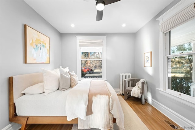 bedroom featuring ceiling fan, radiator, multiple windows, and light hardwood / wood-style flooring