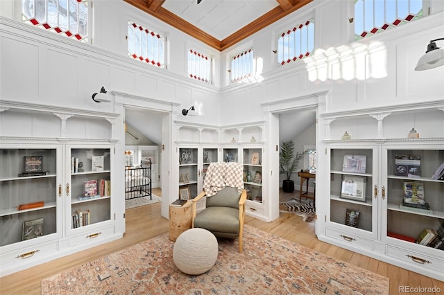 living area featuring crown molding, built in shelves, a high ceiling, and light wood-type flooring