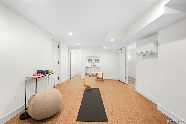 exercise room with a wall mounted AC and light wood-type flooring