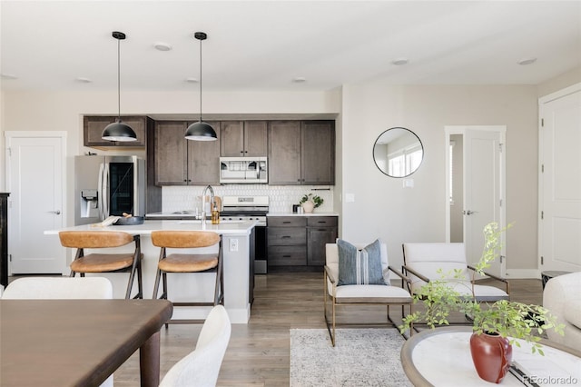 kitchen featuring dark brown cabinetry, tasteful backsplash, hanging light fixtures, an island with sink, and stainless steel appliances