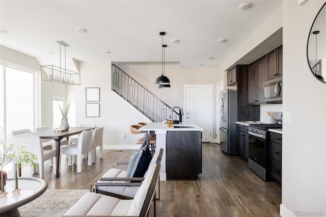 kitchen featuring dark brown cabinetry, sink, appliances with stainless steel finishes, dark hardwood / wood-style flooring, and a kitchen island with sink