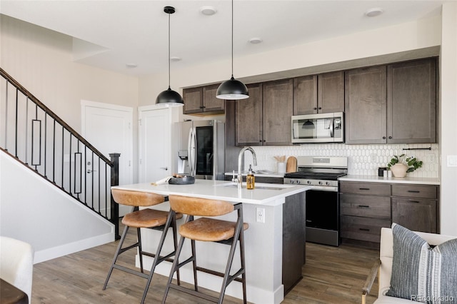 kitchen with sink, stainless steel appliances, dark brown cabinetry, an island with sink, and decorative light fixtures