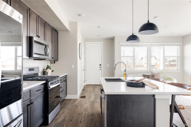 kitchen featuring pendant lighting, sink, appliances with stainless steel finishes, a kitchen island with sink, and dark brown cabinetry