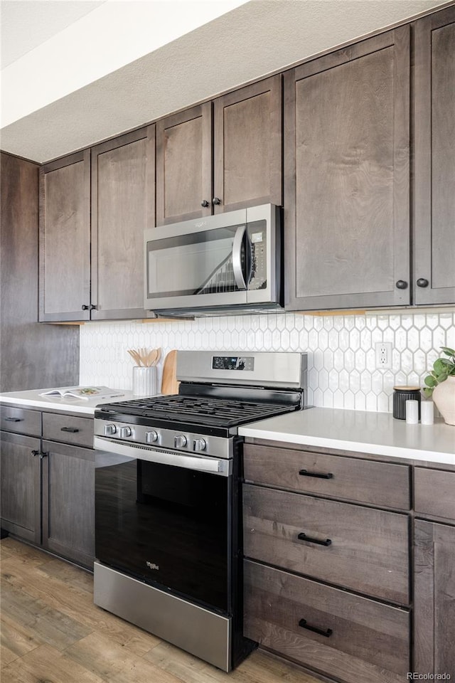 kitchen featuring light hardwood / wood-style flooring, decorative backsplash, dark brown cabinets, and appliances with stainless steel finishes