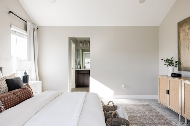 carpeted bedroom featuring ensuite bath and vaulted ceiling