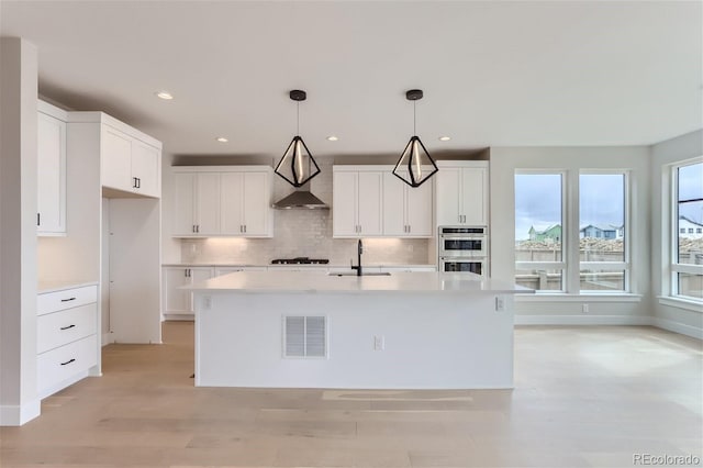 kitchen featuring a kitchen island with sink, hanging light fixtures, sink, and white cabinets