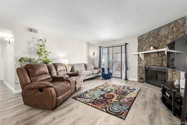 living room with a stone fireplace and light hardwood / wood-style flooring