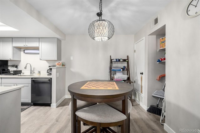 kitchen featuring a notable chandelier, dishwasher, sink, light hardwood / wood-style flooring, and pendant lighting