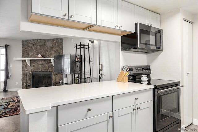 kitchen featuring wood-type flooring, kitchen peninsula, black electric range, white cabinets, and a fireplace