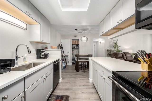 kitchen featuring pendant lighting, sink, white cabinetry, light hardwood / wood-style floors, and black appliances