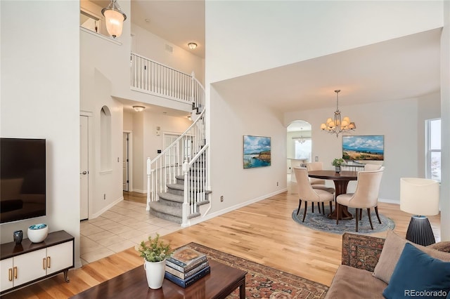 living room featuring light wood-type flooring, a towering ceiling, and an inviting chandelier