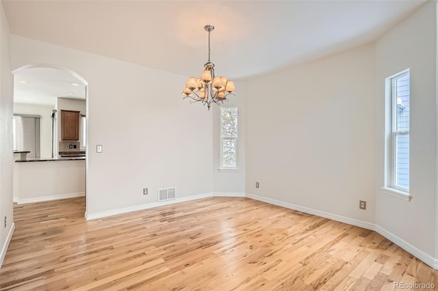 empty room with light hardwood / wood-style flooring, a healthy amount of sunlight, and a notable chandelier