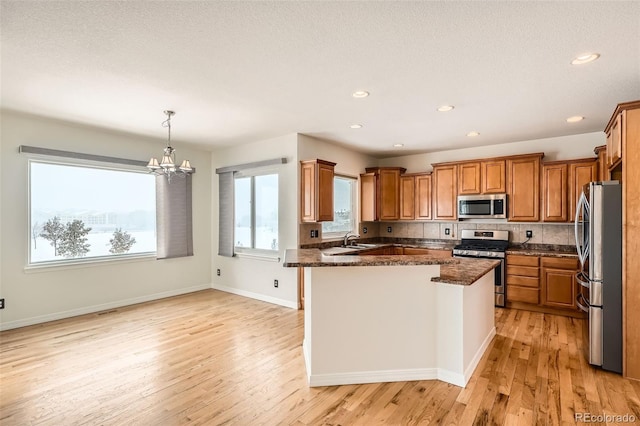 kitchen with sink, hanging light fixtures, stainless steel appliances, dark stone countertops, and light hardwood / wood-style floors