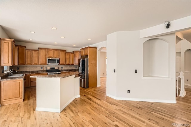 kitchen featuring a center island, backsplash, dark stone counters, light hardwood / wood-style flooring, and appliances with stainless steel finishes