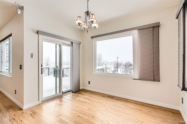 unfurnished room featuring light hardwood / wood-style flooring, a healthy amount of sunlight, and an inviting chandelier