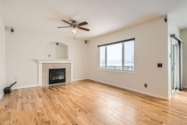 unfurnished living room featuring a tile fireplace, light hardwood / wood-style flooring, and ceiling fan