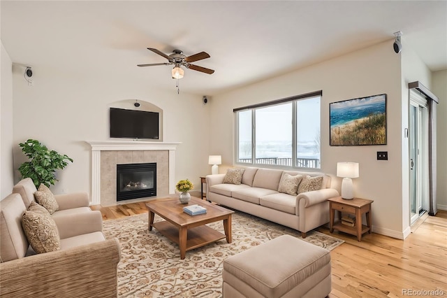 living room featuring a tile fireplace, ceiling fan, and light wood-type flooring