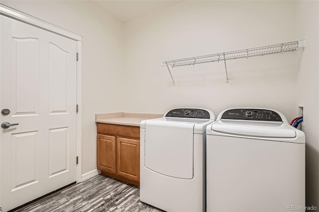 clothes washing area featuring hardwood / wood-style floors, washer and clothes dryer, and cabinets