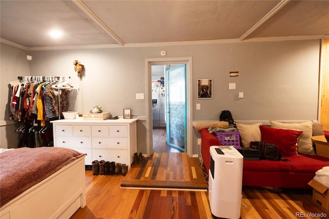 bedroom with wood-type flooring, stainless steel refrigerator with ice dispenser, and ornamental molding