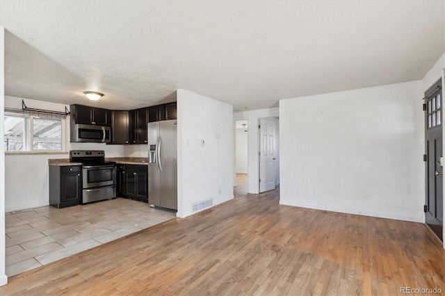 kitchen featuring dark brown cabinets, light wood-type flooring, a textured ceiling, and appliances with stainless steel finishes