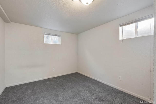 basement featuring a wealth of natural light, a textured ceiling, and dark colored carpet