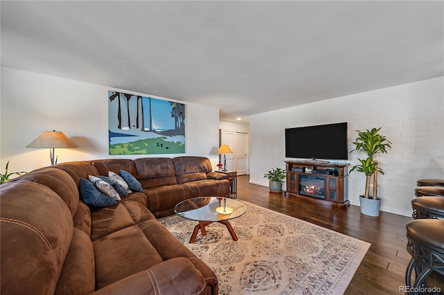 living room featuring a glass covered fireplace, brick wall, and wood finished floors