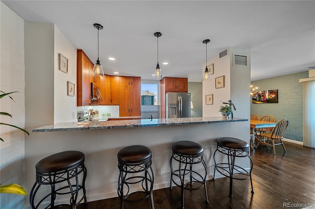 kitchen with stainless steel appliances, stone countertops, brown cabinetry, dark wood-type flooring, and a peninsula