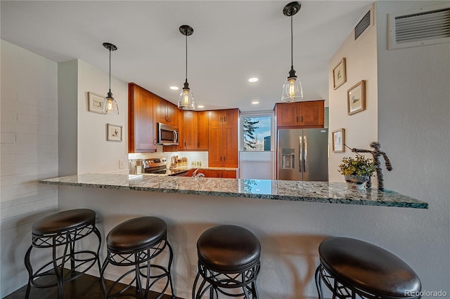 kitchen featuring a peninsula, visible vents, appliances with stainless steel finishes, light stone countertops, and pendant lighting