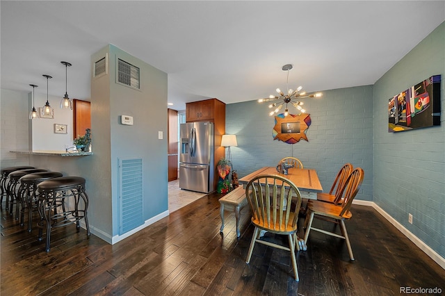 dining space featuring visible vents, dark wood-type flooring, brick wall, a chandelier, and baseboards