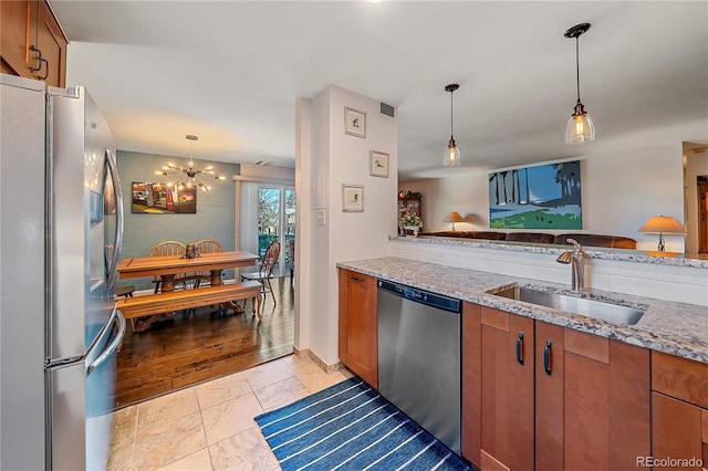 kitchen with brown cabinets, light stone countertops, stainless steel appliances, and a sink