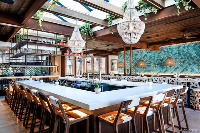 kitchen featuring a spacious island, beamed ceiling, ceiling fan with notable chandelier, and backsplash