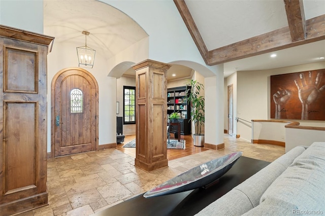 foyer featuring arched walkways, high vaulted ceiling, baseboards, ornate columns, and stone tile flooring