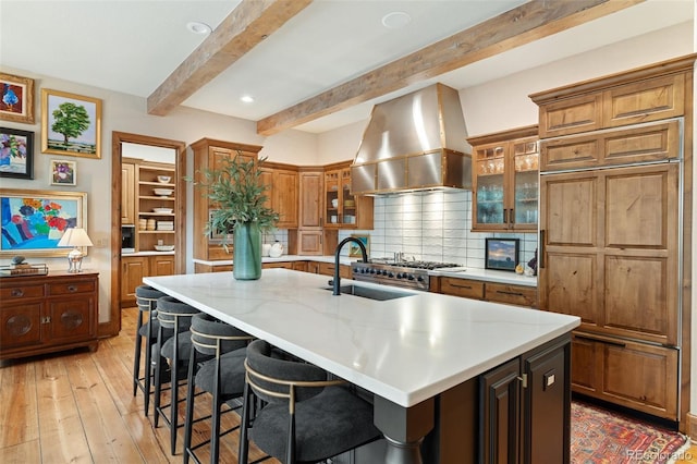 kitchen featuring a kitchen breakfast bar, beamed ceiling, light wood-style flooring, and range hood
