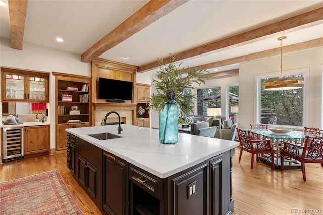 kitchen featuring beam ceiling, a sink, light wood-style floors, light countertops, and wine cooler