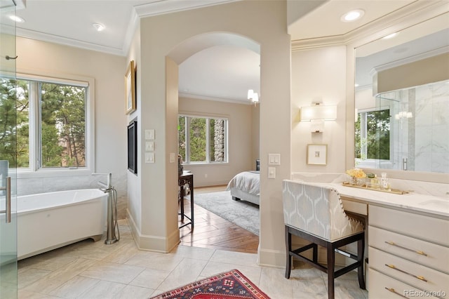 ensuite bathroom with connected bathroom, vanity, baseboards, ornamental molding, and a soaking tub