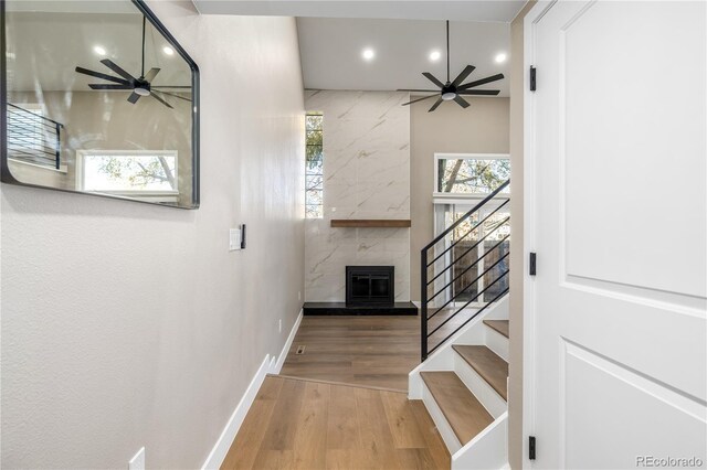 stairway featuring hardwood / wood-style flooring, ceiling fan, and a fireplace