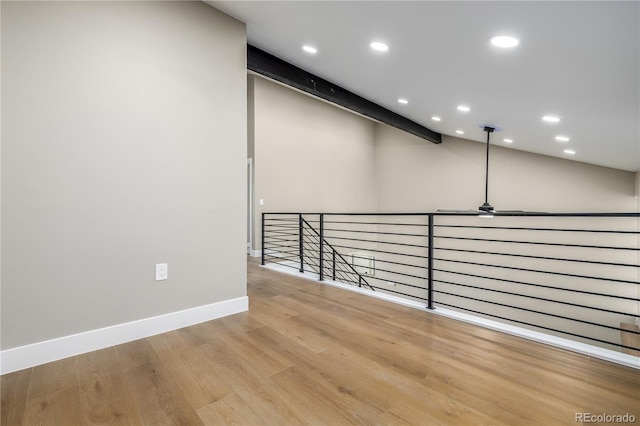 empty room with beamed ceiling, ceiling fan, and light hardwood / wood-style floors