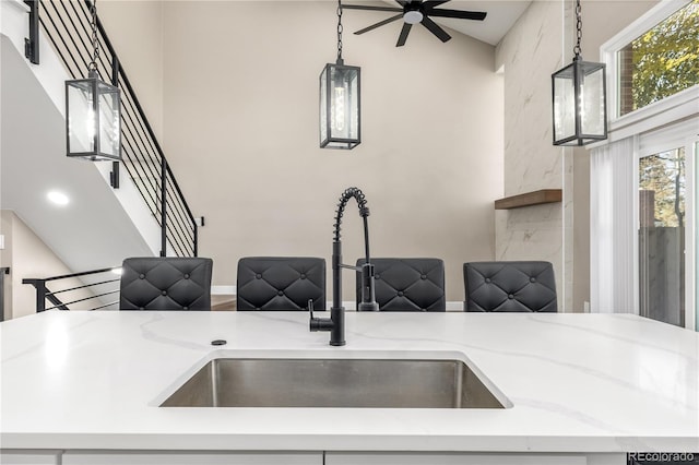 interior space featuring ceiling fan, light stone counters, hanging light fixtures, and sink