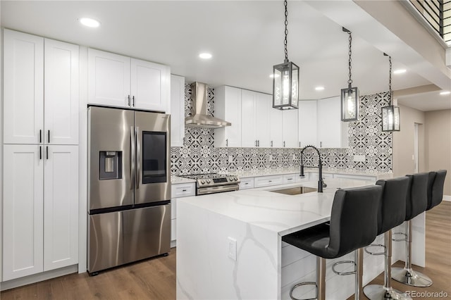 kitchen featuring a kitchen island with sink, wall chimney range hood, sink, appliances with stainless steel finishes, and white cabinetry