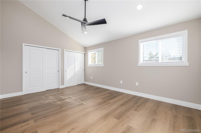 unfurnished bedroom featuring multiple closets, ceiling fan, light hardwood / wood-style flooring, and vaulted ceiling