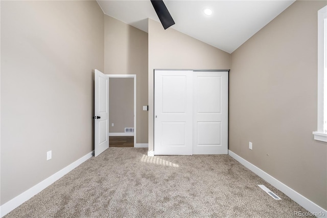 unfurnished bedroom featuring light colored carpet, vaulted ceiling, a closet, and ceiling fan