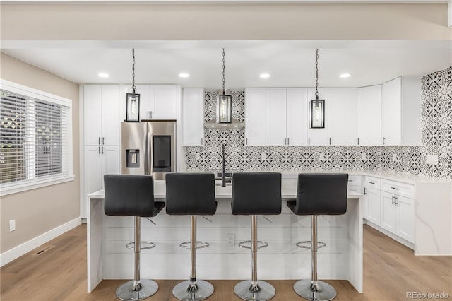 kitchen with stainless steel fridge, a kitchen breakfast bar, decorative light fixtures, white cabinets, and a center island