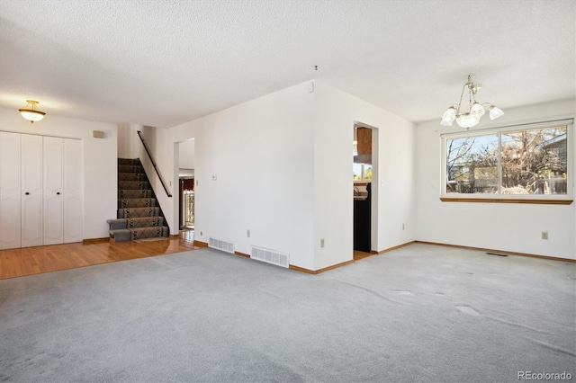 unfurnished living room featuring a notable chandelier, wood-type flooring, and a textured ceiling