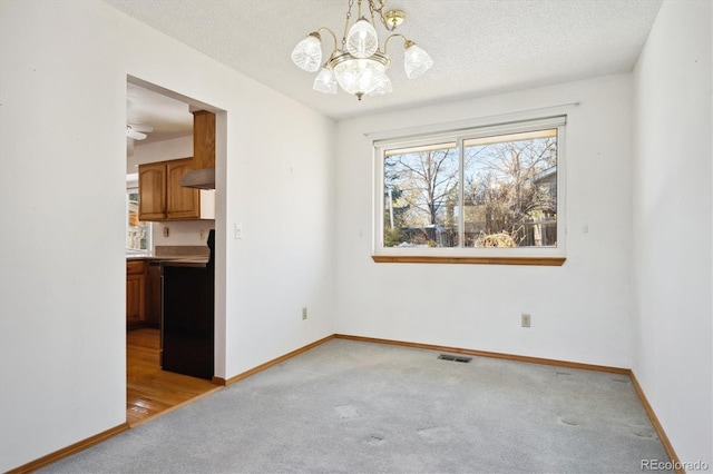 empty room featuring a chandelier, light colored carpet, and a textured ceiling