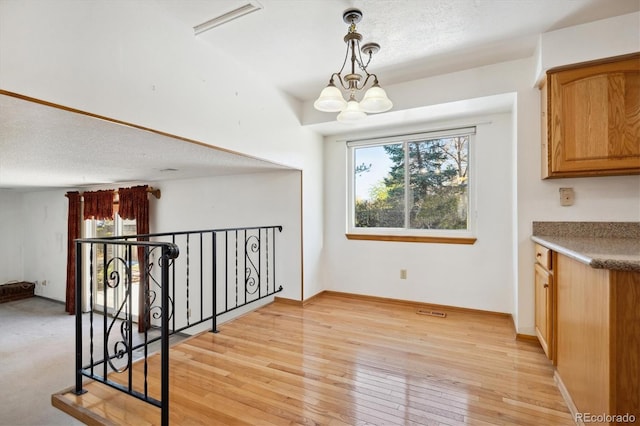 unfurnished dining area featuring a chandelier, a textured ceiling, and light wood-type flooring