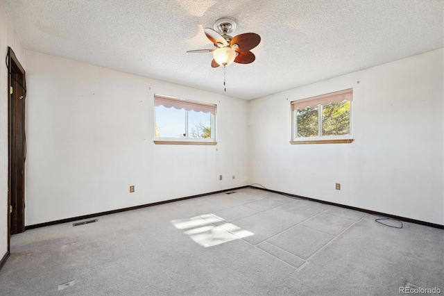 empty room with a textured ceiling, light colored carpet, ceiling fan, and a healthy amount of sunlight