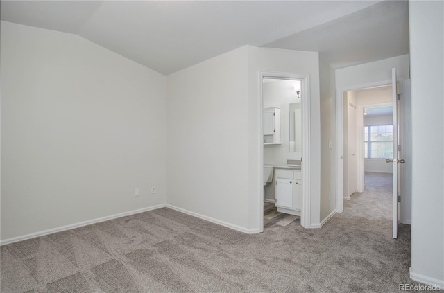 unfurnished bedroom with connected bathroom, light colored carpet, and vaulted ceiling