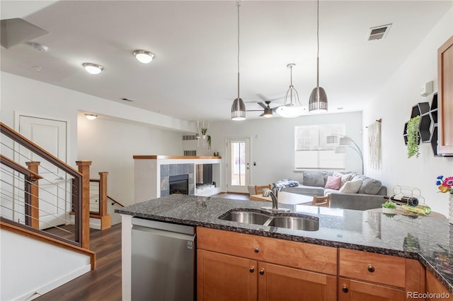 kitchen with brown cabinetry, visible vents, a sink, stainless steel dishwasher, and open floor plan