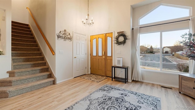 foyer entrance featuring stairway, wood finished floors, visible vents, an inviting chandelier, and a towering ceiling